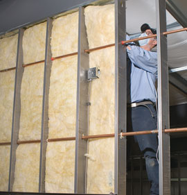Technician wearing facemask and installing batt metal building insulation.