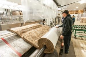 Faced wide-roll insulation blanket being rolled up by a technician