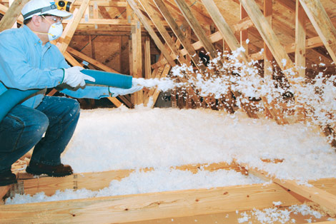 Technician blowing in white loose-fill insulation in an attic.