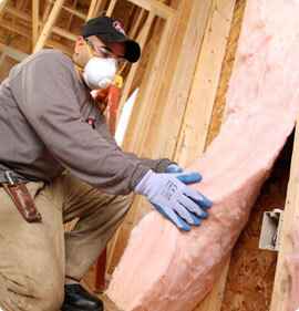 A technician installing fiberglass batt insulation into a wall
