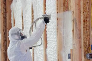 Technician in hazmat suit, applying spray foam insulation to a wall.