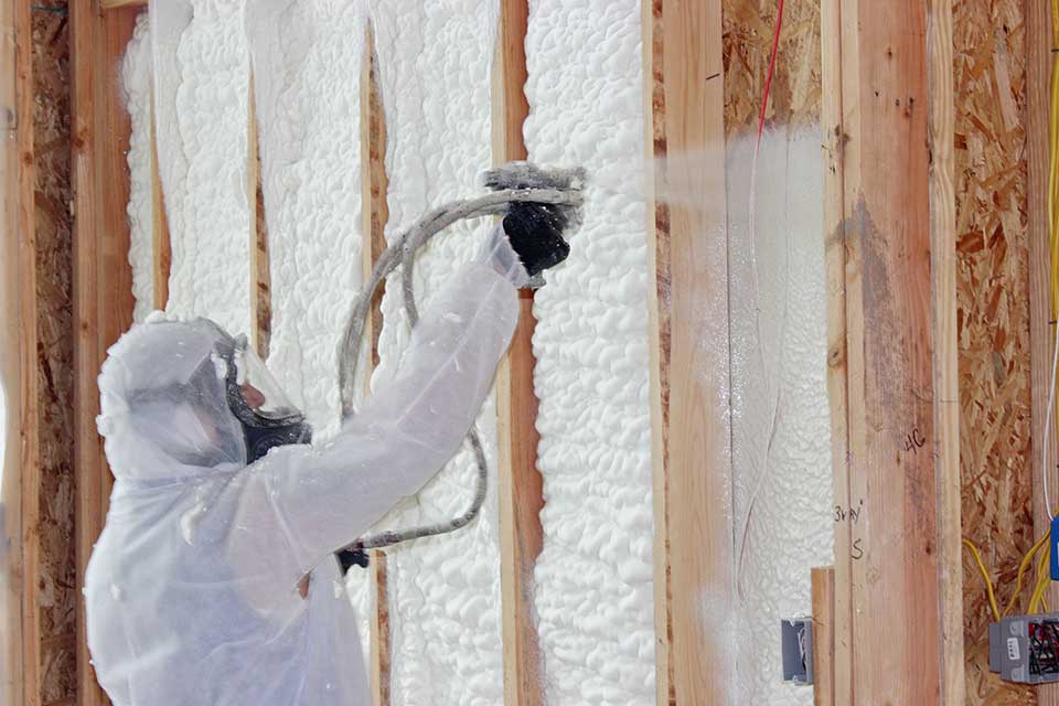 Technician in white hazmat suit, installing spray foam insulation in an unfinished wall.