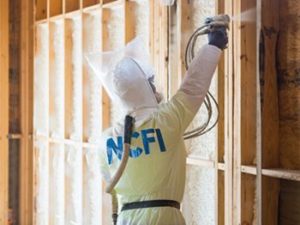 Technician in hazard suit, installing spray foam insulation in a wall.