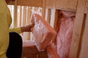 Technician installing a piece of pink fiberglass batt insulation in a wall.